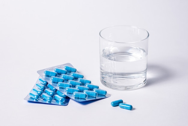 Due confezioni di capsule blu e un bicchiere d'acqua. Pillole per la salute e l'energia sessuale degli uomini. Concetto di erezione, potenza. Trattamento di infertilità maschile e impotenza e prostatite.