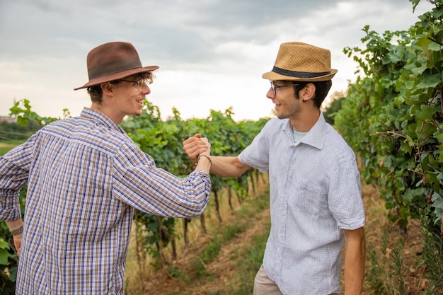 Due contadini si stringono la mano e sono felici mentre stanno in piedi nel vigneto