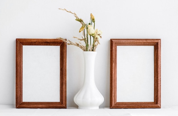 Due cornici in legno con un inserto bianco all'interno e fiori secchi bianchi in un vaso bianco Cornice per foto su sfondo bianco