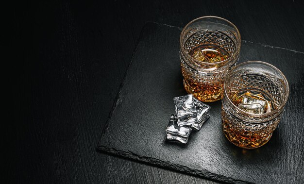 Due costosi bicchieri di whisky con ghiaccio su un vassoio di pietra nera