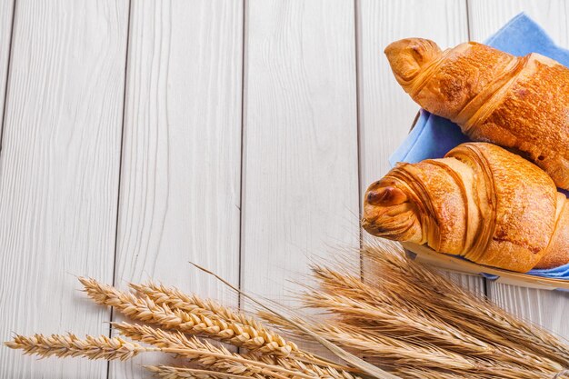 Due croissant e spighe di grano su vecchie tavole di legno bianche con copyspace