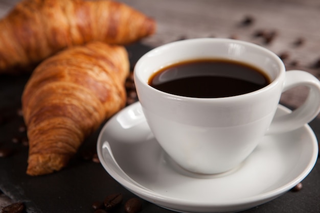 Due croissant freschi e una tazza di caffè sul tavolo di pietra scura. Dolce delizioso.