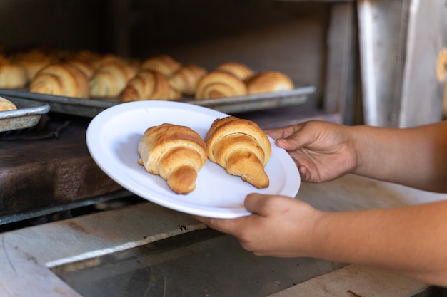 Due croissant in un piatto nelle mani di una persona davanti a un forno