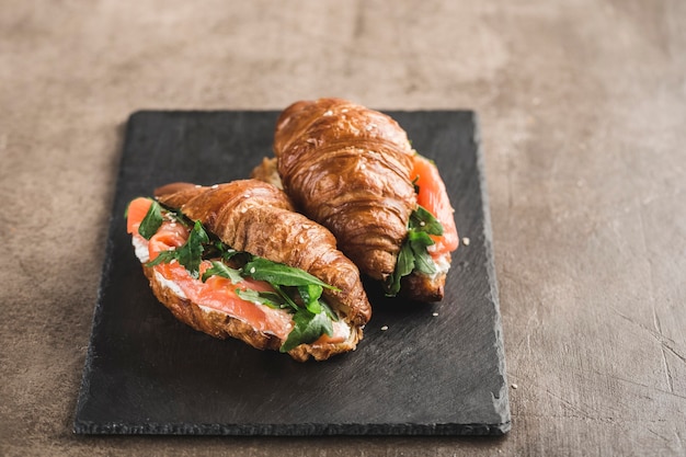 Due croissant sandwich con salmone, ricotta e rucola su una tavola di ardesia nera