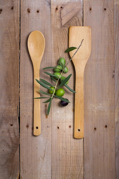 Due cucchiai di legno con olive e un ramo d'ulivo verde sopra.