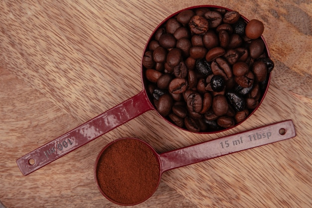 Due cucchiai rossi con chicchi di caffè e caffè macinato