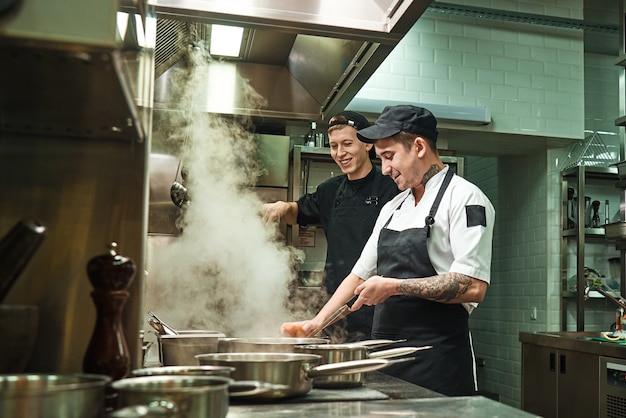 due cuochi allegri e sorridenti in uniforme stanno preparando un cibo in un ristorante di cucina