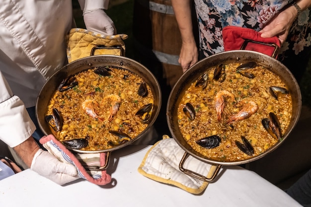 Due cuochi con paella di frutti di mare, cucina mediterranea tradizionale spagnola. Riso con cozze, gamberi e calamari