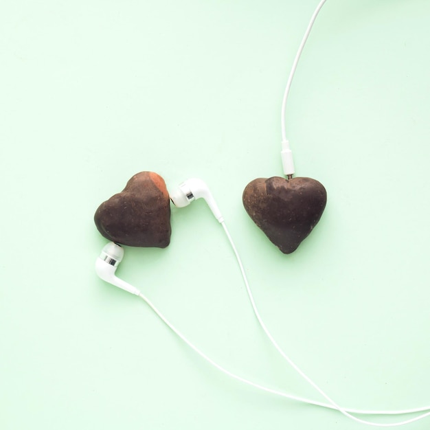 Due cuori di cioccolato hanno collegato le cuffie bianche su sfondo verde, piatto