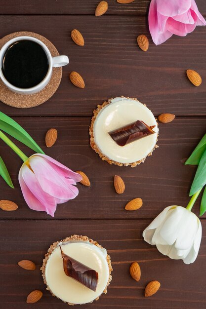 Due cupcakes con cioccolato bianco tazza di caffè mandorla e tulipani su tavola di legno Piatto