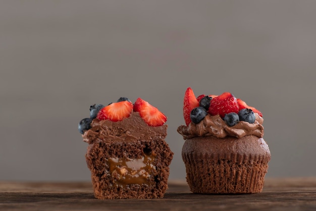 Due cupcakes freschi con cioccolato e frutti di bosco Muffin tagliato con panna e frutta sul tavolo di legno Sfondo grigio