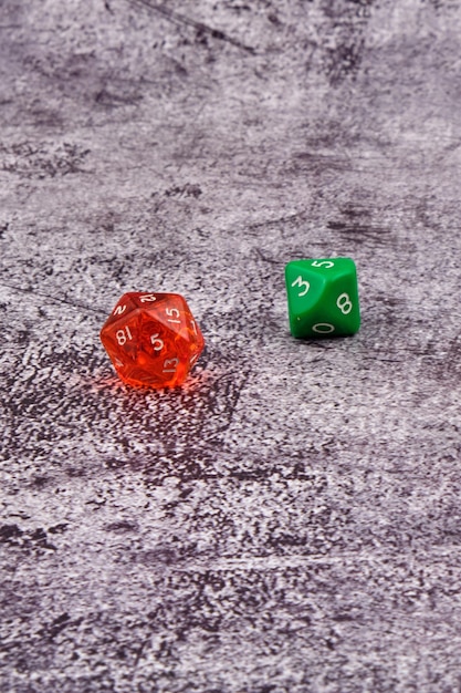 Due dadi per giochi di ruolo, uno rosso e uno verde, sopra un tavolo di cemento.