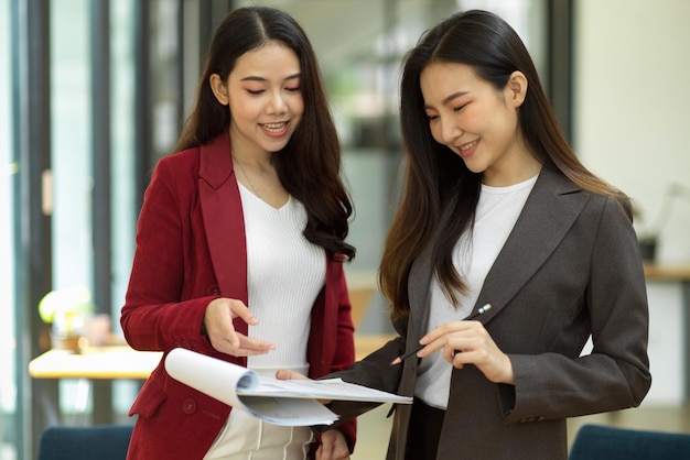 Due dei bei colleghi di lavoro asiatici che guardano insieme il foglio di calcolo dei dati aziendali in ufficio. discutere, parlare o fare un brainstorming.