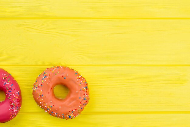 Due deliziose ciambelle su fondo di legno giallo. Ciambelle con confettini colorati. Spazio per il testo.