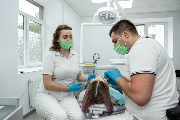 due dentisti un uomo e una donna trattano i denti malati di una bella paziente donna che tiene la bocca aperta denti di salute orale