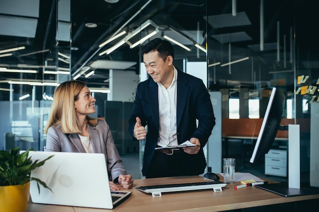 Due dipendenti in un ufficio moderno un uomo asiatico e una donna che lavorano a un tavolo colleghi che discutono e si consultano pensando a un progetto comune