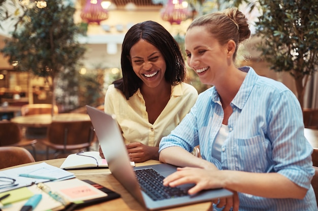 Due diverse giovani donne d'affari che ridono mentre lavorano insieme su un laptop a un tavolo