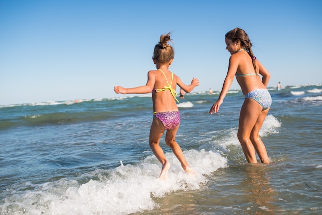 Due divertenti bambine saltano tra le rumorose onde del mare e si godono la tanto attesa vacanza in una soleggiata giornata estiva calda