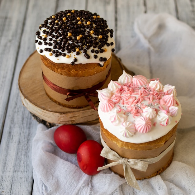 Due dolci pasquali. Il pane dolce tradizionale di Pasqua ha decorato la meringa, le gocce di cioccolato, le uova rosse su fondo di legno con il tessuto di lase. Copia spazio, messa a fuoco selettiva