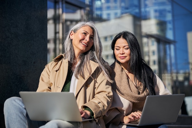 Due donne affascinanti che usano i laptop per strada