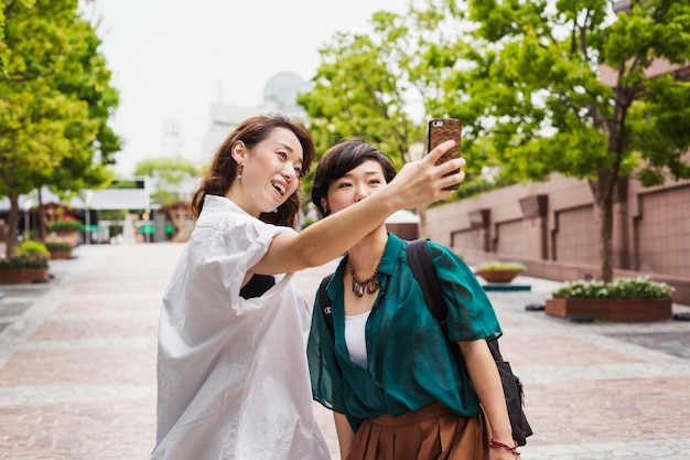 Due donne all'aperto che scattano foto con il cellulare sorridente