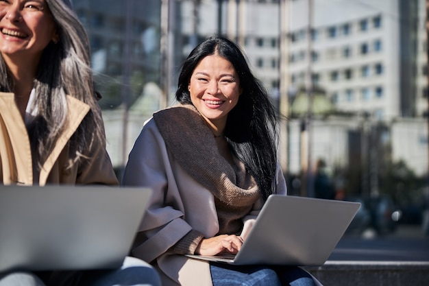 Due donne allegre che usano laptop moderni all'aperto