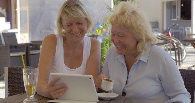 Due donne anziane che guardano le foto sul pad in street cafe