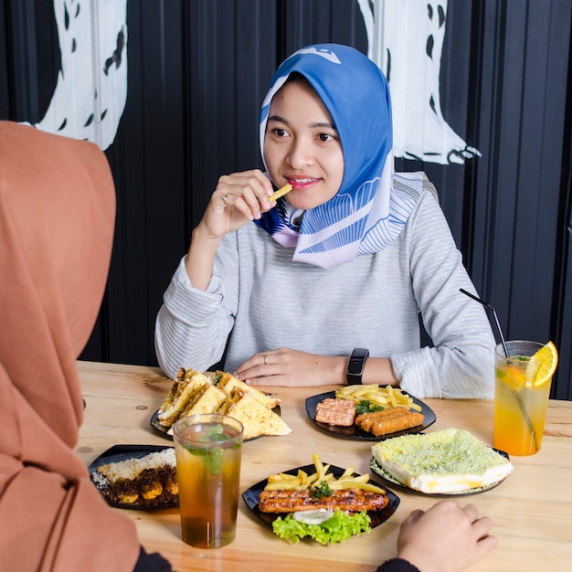 due donne asiatiche hijab mangiano il loro cibo e ridono con i loro amici al ristorante della folla
