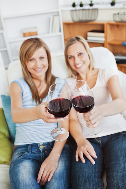 Due donne brillanti in possesso di un bicchiere di vino su un divano