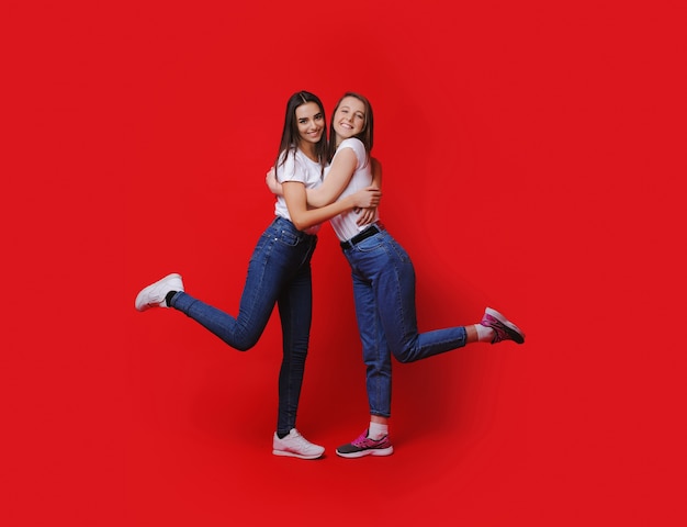 Due donne caucasiche allegre che si abbracciano e sorridono felicemente su uno sfondo rosso freespaced