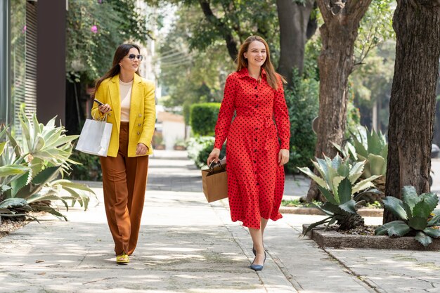 Due donne caucasiche felici che fanno shopping in città portando le borse dei loro acquisti