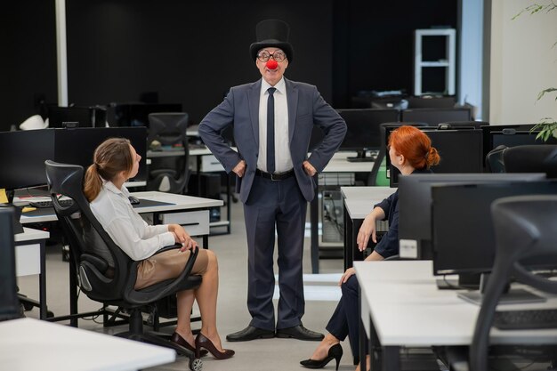 Due donne caucasiche sedute in ufficio e che guardano un clown.