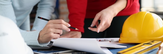 Due donne che guardano i documenti e li mostrano a matita nel coordinamento dello studio del design