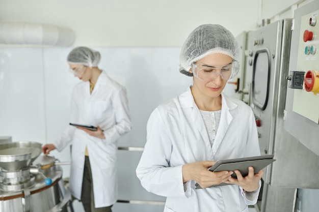 Due donne che indossano camicie da laboratorio che lavorano in una fabbrica di prodotti alimentari o farmaceutici