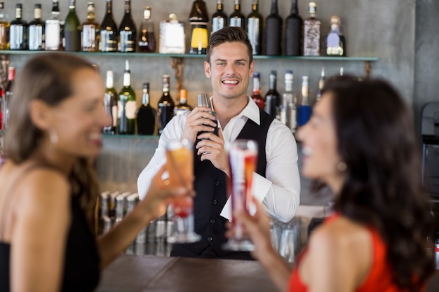 Due donne che mangiano cocktail mentre un cameriere che prepara cocktail con l'agitatore di cocktail