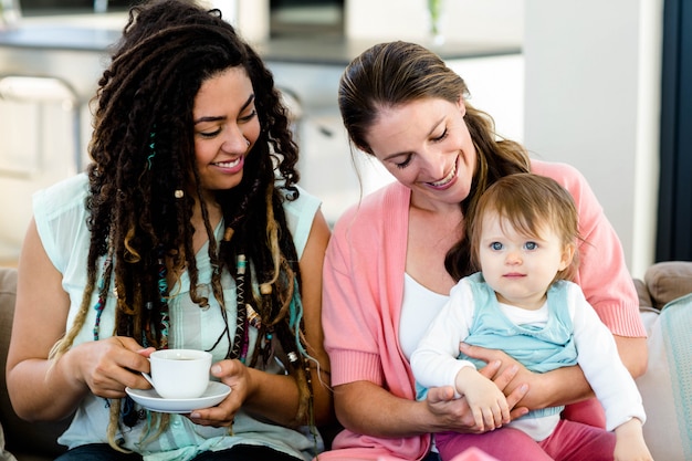 Due donne che sorridono e che si siedono sul sofà con un bambino