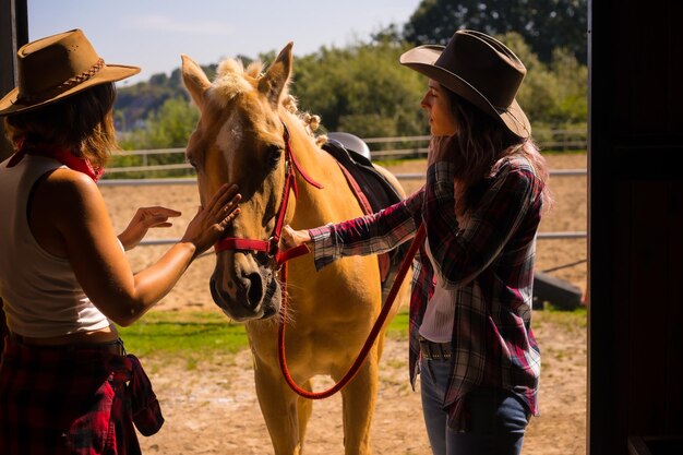 Due donne cowgirl entrano nella stalla con un cavallo su un cavallo, con abiti sudamericani