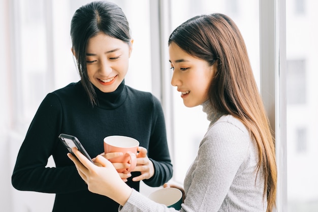 Due donne d'affari asiatiche stavano chiacchierando vicino alla finestra durante la ricreazione