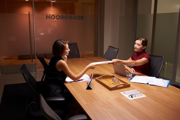 Due donne d'affari che lavorano fino a tardi in ufficio passando i documenti