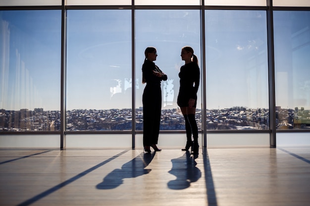 Due donne d'affari che si godono la vista della città e parlano mentre sono in piedi accanto alla grande finestra dell'ufficio