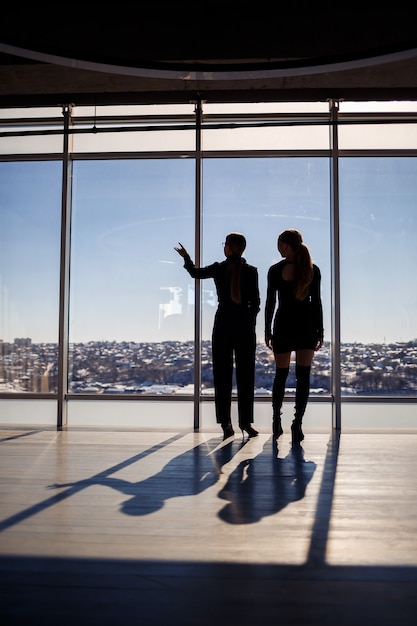 Due donne d'affari che si godono la vista della città e parlano mentre sono in piedi accanto alla grande finestra dell'ufficio