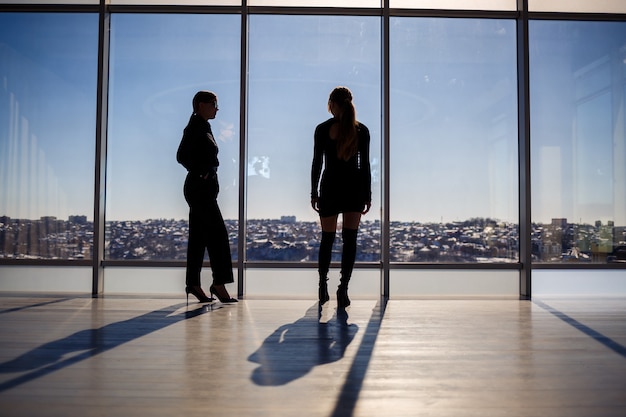 Due donne d'affari che si godono la vista della città e parlano mentre sono in piedi accanto alla grande finestra dell'ufficio