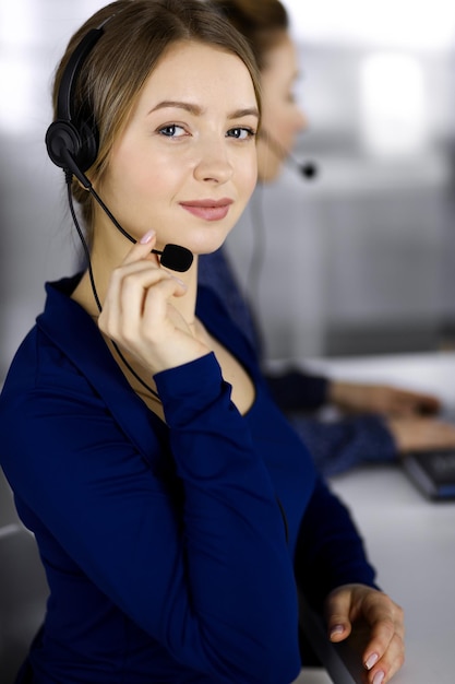 Due donne d'affari conversano con i clienti tramite cuffie, mentre sono sedute alla scrivania di un ufficio moderno. Diverse persone raggruppano in un call center. Telemarketing e servizio clienti.