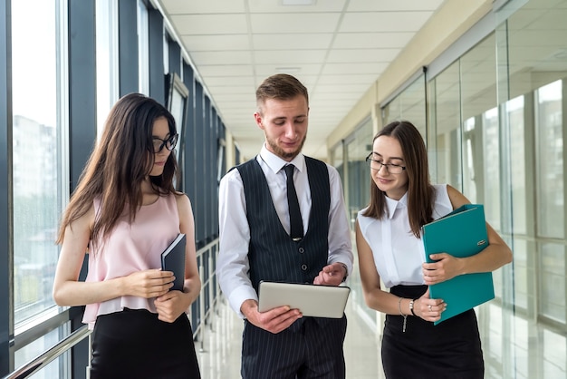 Due donne d'affari e un uomo seri mostrano un documento e parlano di errori da subordinare nel corridoio dell'ufficio. Concetto di riunione