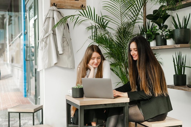 Due donne d'affari sorridenti che si siedono nella caffetteria e che lavorano al computer guardando lo schermo del laptop