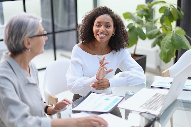 Due donne d'affari sorridono mentre lavorano insieme su un laptop a un tavolo nella sala riunioni dell'ufficio