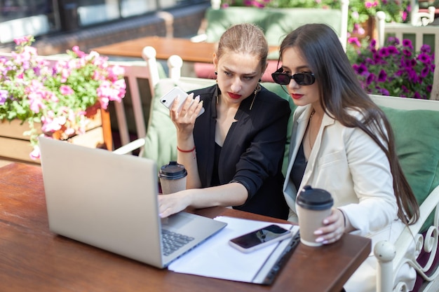 Due donne d'affari stanno studiando informazioni importanti mentre guardano lo schermo del laptop mentre sono sedute al tavolo in un bar