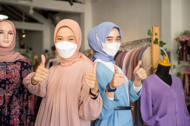 Due donne d'affari velate che indossano maschere con i pollici in su mentre stanno una dietro l'altra