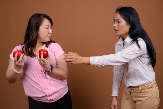 Due donne di affari asiatiche mature insieme contro la parete marrone