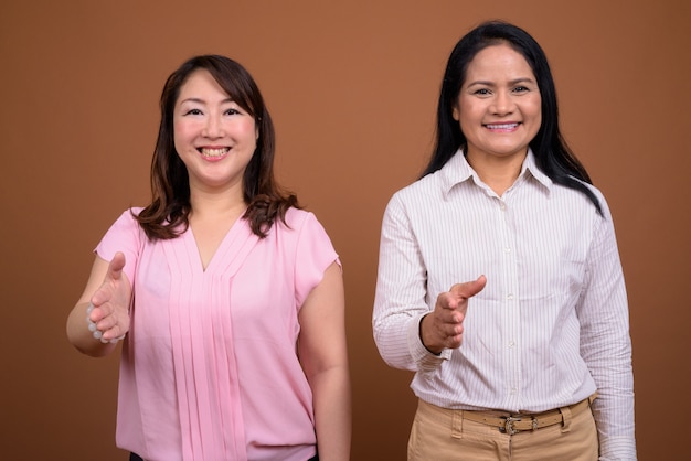 Due donne di affari asiatiche mature insieme contro la parete marrone